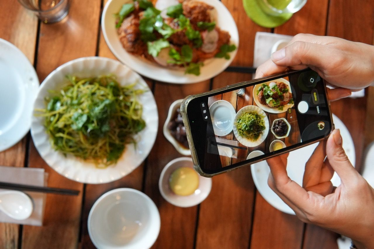 Mano fotografiando con el celular una mesa con platillos de Makan